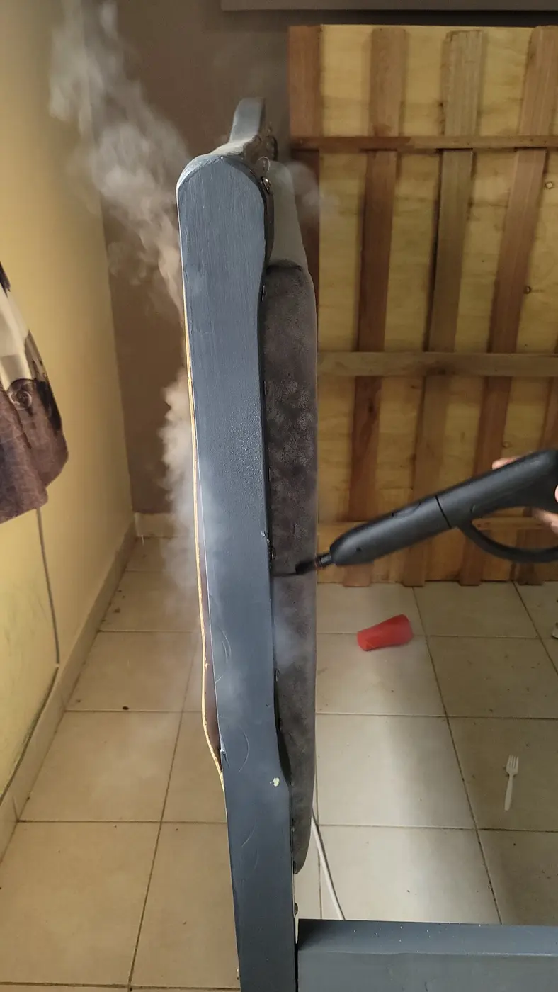 Visible steam applied along an upholstered bed edge during bedbug treatment